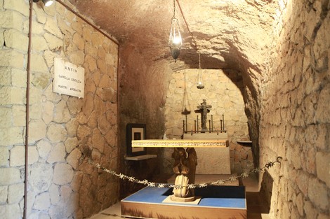 Interno della Cappella delle Fosse Ardeatine, con pareti in pietra e altare centrale in legno. Atmosfera solenne e commemorativa.