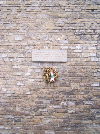 Lapide commemorativa su muro di pietra con corona d'alloro, dedicata ai caduti presso Porta al Prato.