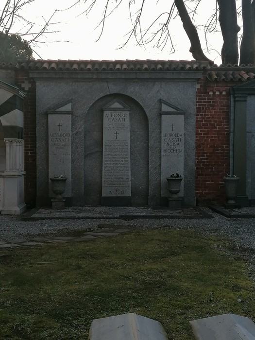 Mausoleo Casati con iscrizioni commemorative, circondato da un giardino curato. Atmosfera di quiete e riflessione.
