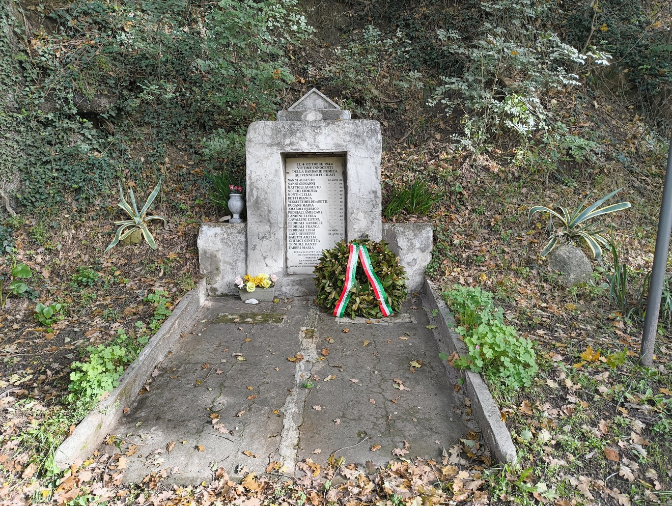 Monumento dedicato agli uccisi di Ca' di Beguzzi, con vasi e fiori commemorativi in un ambiente naturale.