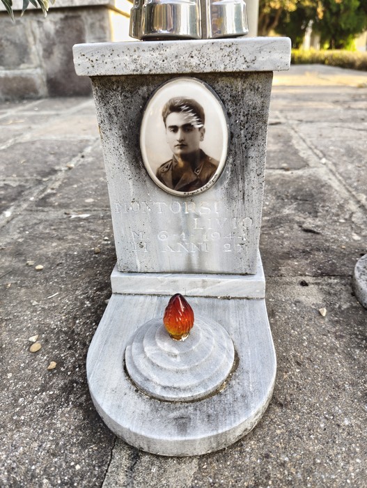 Monumento commemorativo con una foto in bianco e nero e un oggetto rosso in cima, dedicato ai caduti.
