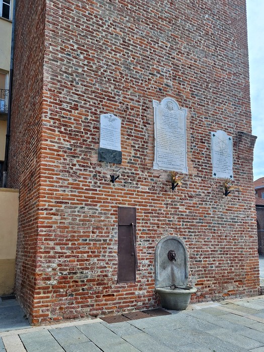 Lapide commemorativa in muratura, dedicata ai caduti per la libertà, con fontana sottostante e dettagli architettonici.