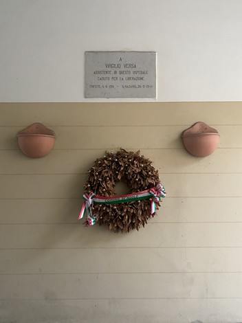 Lapide commemorativa dedicata a Virgilio Versa, con una corona di alloro decorata.