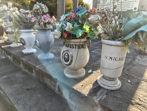 Vasi di fiori artificiali su una struttura commemorativa in memoria dei caduti, con nomi visibili.