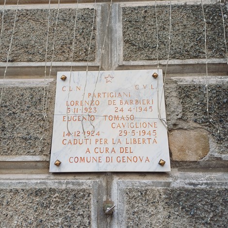 Lapide marmorea con iscrizione, fissata a parete in pietra con viti visibili agli angoli.