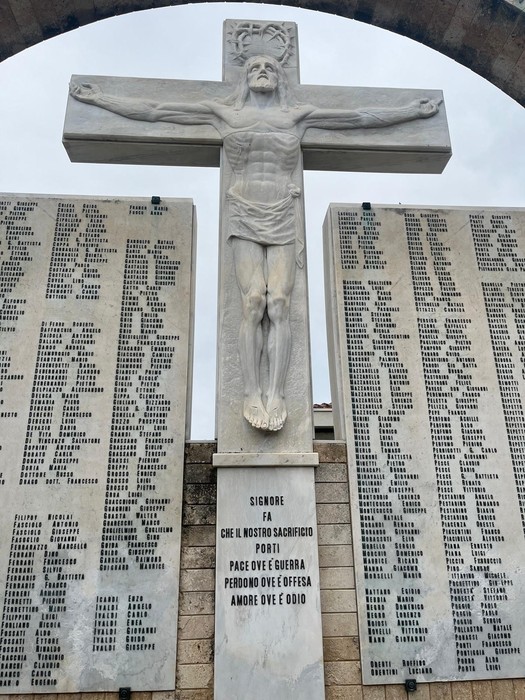Statua di Cristo crocifisso con dipinti commemorativi e iscrizioni, simbolo di memoria e pace.