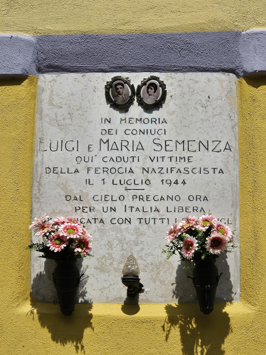 Lapide commemorativa dedicata ai coniugi Semenza, con fiori e immagini, in memoria delle vittime della ferocia nazifascista.