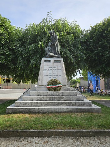 Il Monumento ai Caduti di Solarolo Rainerio, con statue e una corona d'alloro, immerso nel verde.