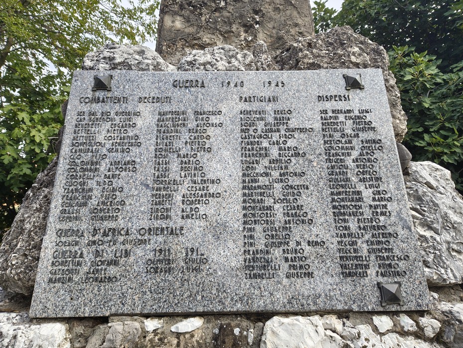 Lapide in granito con lunghe liste di nomi incisi, fissata su un masso roccioso all'aperto.