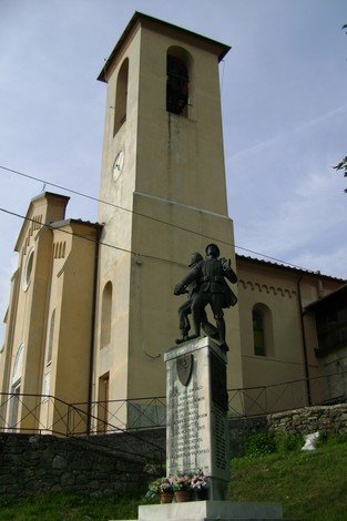 Monumento ai caduti di Sassalbo, con statue commemorative e chiesa sullo sfondo.