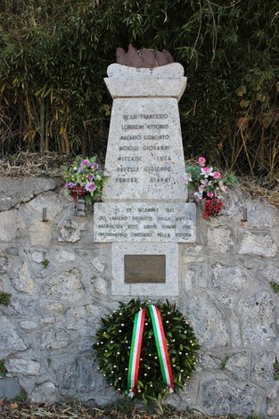 Monumento commemorativo ai Tredici Martiri, con decorazioni floreali e una corona d'alloro, su sfondo di massi.