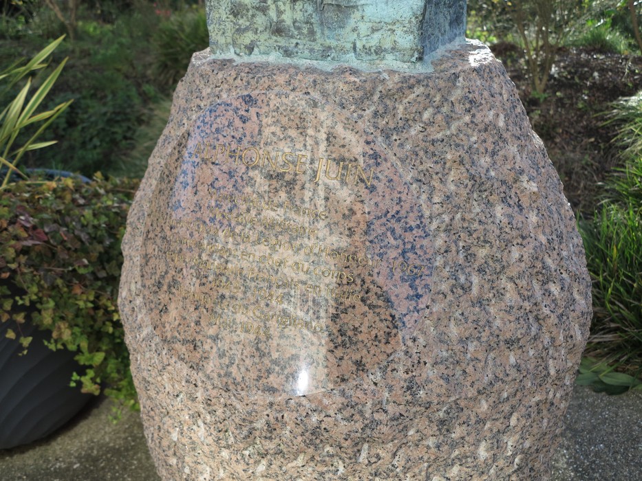 Busto commemorativo di Juin, composto da bronzo e posto su una base di pietra, immerso in un contesto verde.