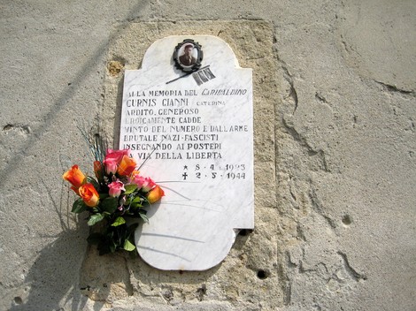 Lapide commemorativa a Curnis in memoria di Gianni Curnis, con fiori e dedica alla libertà.