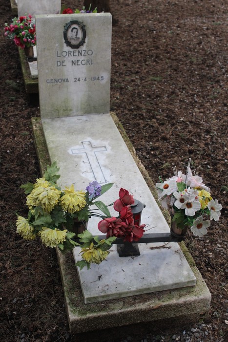 Tomba decorata con fiori in memoria di Lorenzo De Negri, con croce e fotografia commemorativa.