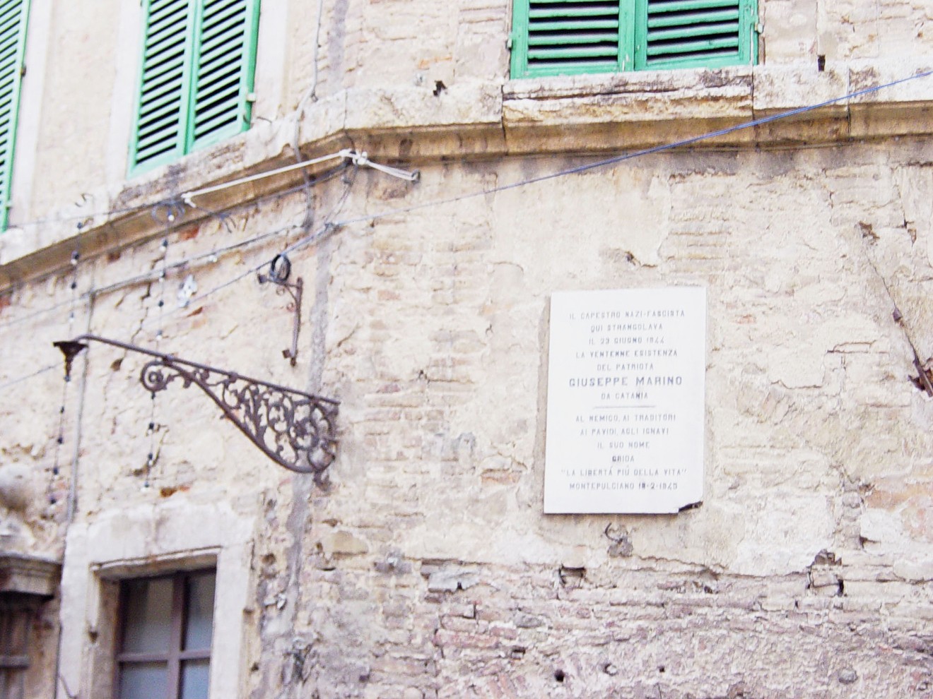 Lapide commemorativa a Marino, affissa su un muro di una palazzina storica, con finestre verdi.