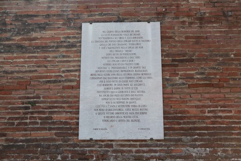 Lapide commemorativa dedicata alle vittime del Porrajmos, collocata su un muro di mattoni.