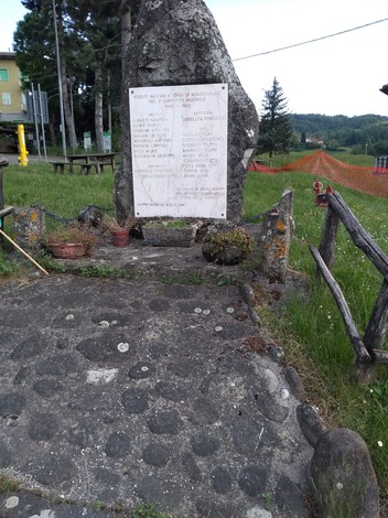 Monumento ai caduti di Montecorone, situato in un'area verde circondata da alberi e una recinzione in legno.