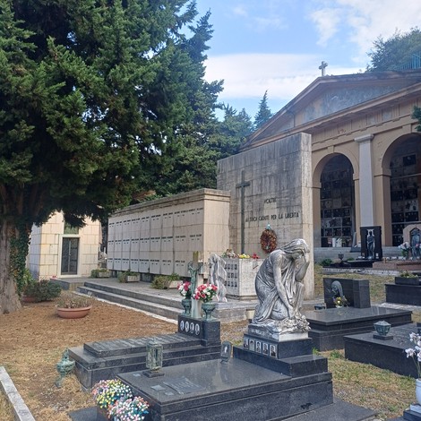 Cimitero monumentale con sacrario dei partigiani, statue, loculi e lapidi con iscrizioni tra alberi.