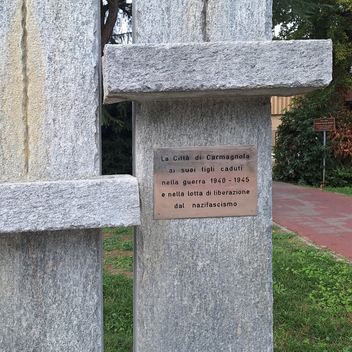 Targa in metallo con iscrizione su un pilastro di pietra, in un monumento all'aperto.