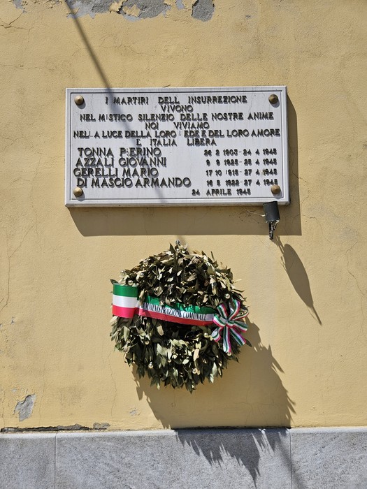 Lapide commemorativa dedicata ai Martiri dell'Insurrezione, con una corona di alloro e decorazioni tricolori.