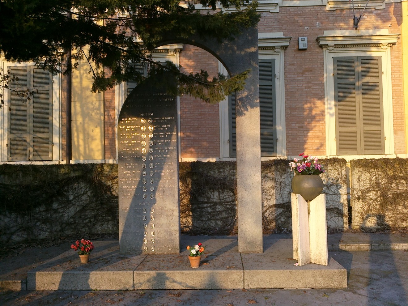 Monumento ai Caduti di Massenzatico, commemorazione in granito con fiori ai piedi, situato in un'area tranquilla.
