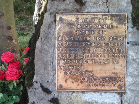 Monumento della fossa comune dedicato a patrioti cremonesi caduti per la libertà, con fiori rossi ai piedi.