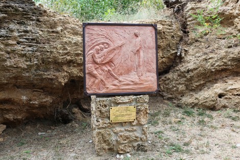 Monumento a Don Bortolotti, incastonato in un contesto naturale, rappresenta figure simboliche su rilievo.
