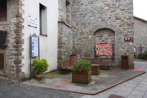 Monumento commemorativo in pietra dedicato alle vittime della strage di Moggiona, con panchine e piante circostanti.