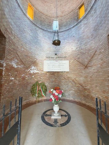 Interno del Sacrario ai Caduti Partigiani di Piumazzo, con decorazioni floreali e una lapide commemorativa.