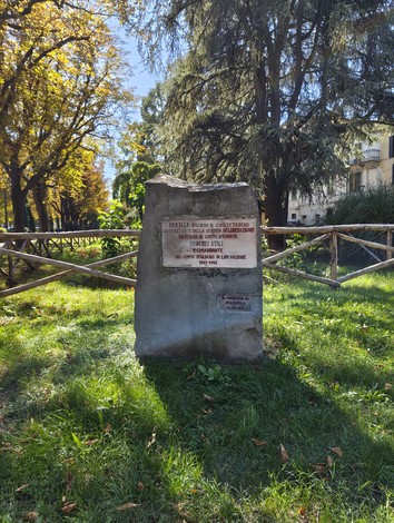 Cippo in pietra con targa e iscrizione, collocato in un parco alberato.