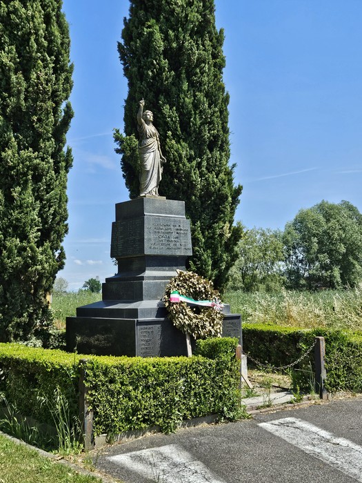 Monumento ai Caduti di Cingia de' Botti circondato da cipressi e un'aiuola verde, con una corona di fiori.