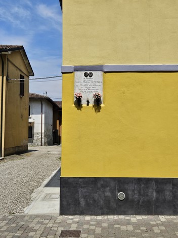 Lapide commemorativa sui coniugi Semenza affissa a un muro giallo in un'area residenziale.