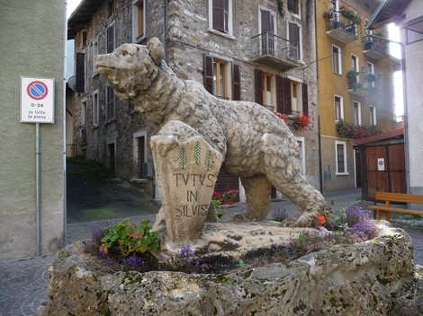 Lapide commemorativa con simbolo di un'orsa, situata in un contesto urbano di montagna.