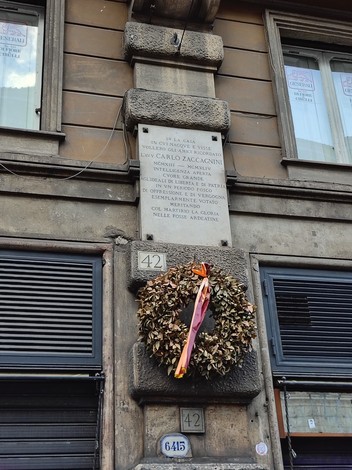 Lapide commemorativa dedicata a Carlo Zaccagnini, affissa su un muro con corona di foglie e nastri decorativi.
