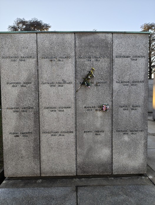 Memoriale commemorativo con lapidi in pietra, adornate da fiori freschi e ricordi personali.