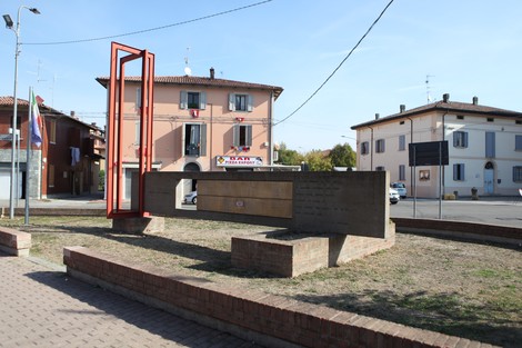 Monumento ai Caduti di Manzolino, struttura commemorativa in un'area pubblica, circondata da edifici e strada.