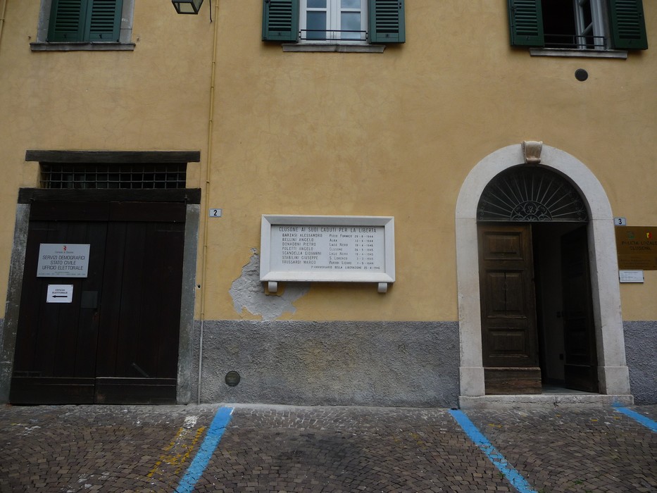 Lapide commemorativa dedicata ai partigiani caduti, posta su una parete in un contesto urbano.