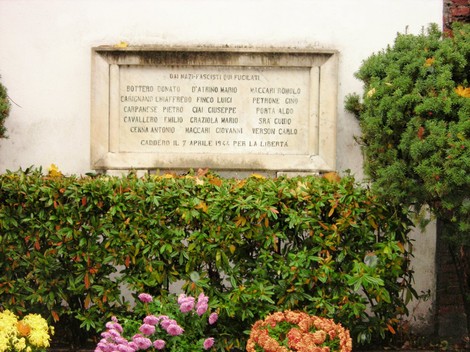 Lapide commemorativa dedicata ai fucilati di Caluso, situata in un contesto floreale.
