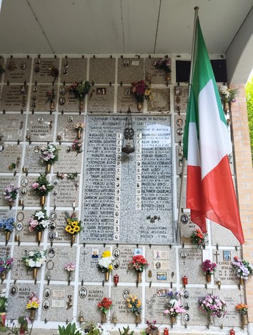 Lapide commemorativa con nomi dei caduti per la Libertà, decorata con fiori e bandiera italiana.