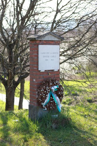 Lapide commemorativa a Dovesi, con una corona di fiori e un albero sullo sfondo.