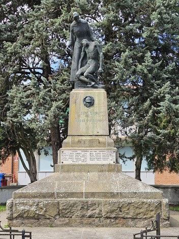 Monumento ai Caduti di Arquà Polesine, con statua centrale e iscrizioni commemorative. Circondato da alberi.