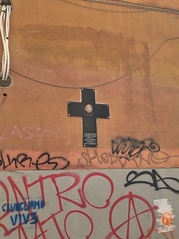 Croce commemorativa per i bombardamenti di San Lorenzo, collocata su una parete decorata da graffiti.