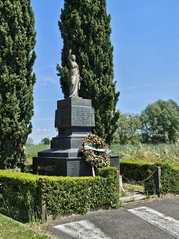 Monumento ai Caduti di Cingia de' Botti circondato da cipressi e un'aiuola verde, con una corona di fiori.