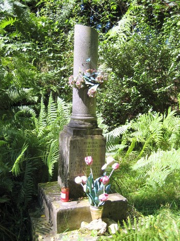 Cippo a Predebon, monumento circondato da vegetazione, adornato di fiori e candele.