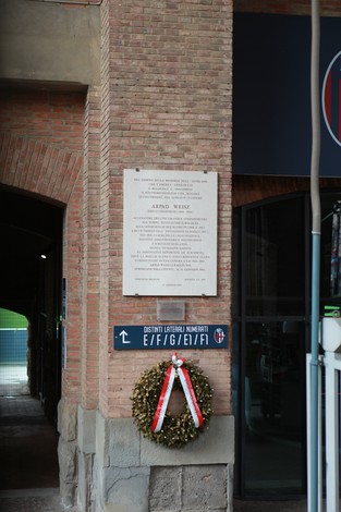 Lapide commemorativa a Weisz con corona di fiori, situata in un edificio caratteristico.