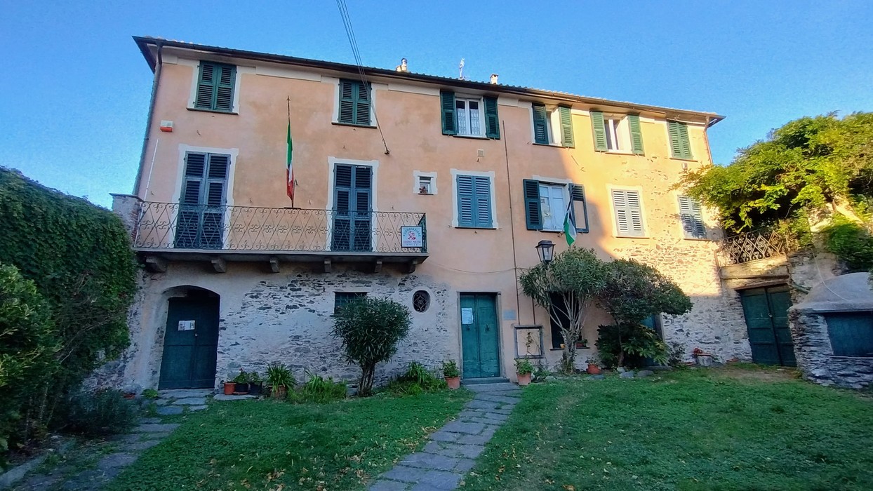 Edificio storico con facciata color pastello, balconi, finestre con persiane e giardino curato.
