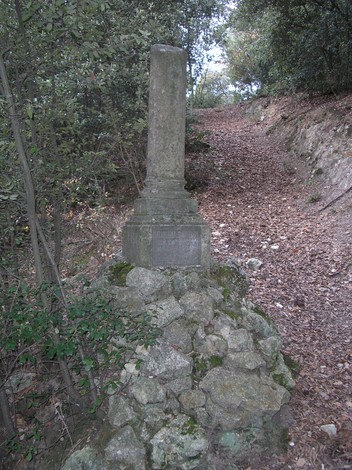 Cippo commemorativo immerso nella vegetazione, visibile lungo un sentiero naturale.