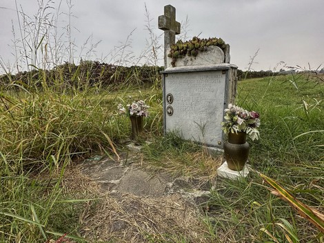 Cippo funerario di Ronzoni e Ori, circondato da erba e fiori, in un contesto rurale.