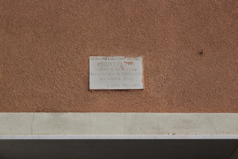 Lapide commemorativa dedicata a Perini, affissa su un muro di colore ocra.
