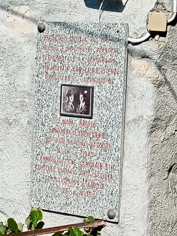 Lapide in marmo su parete esterna, con foto di due uomini e lunga iscrizione dedicatoria.